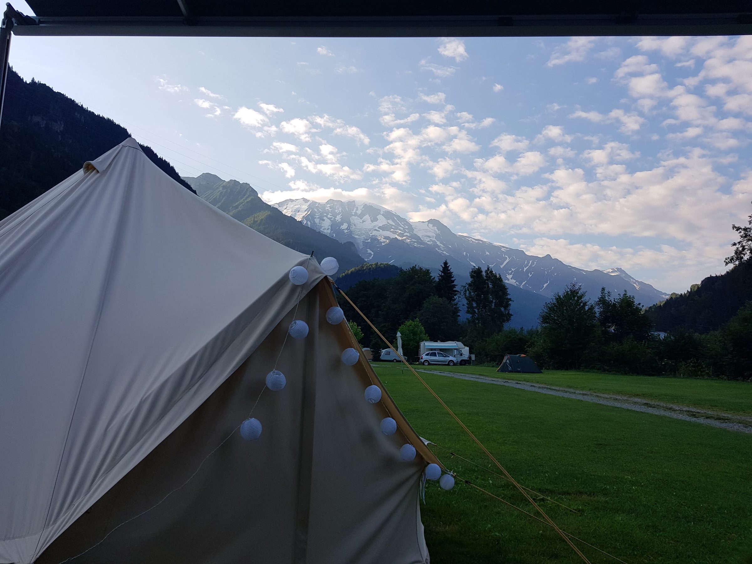 A canvas bell tent hung with paper lanterns on the grass at Les Dômes de Miage campsite, with the snow-streaked Dômes de Miage rising beyond the trees