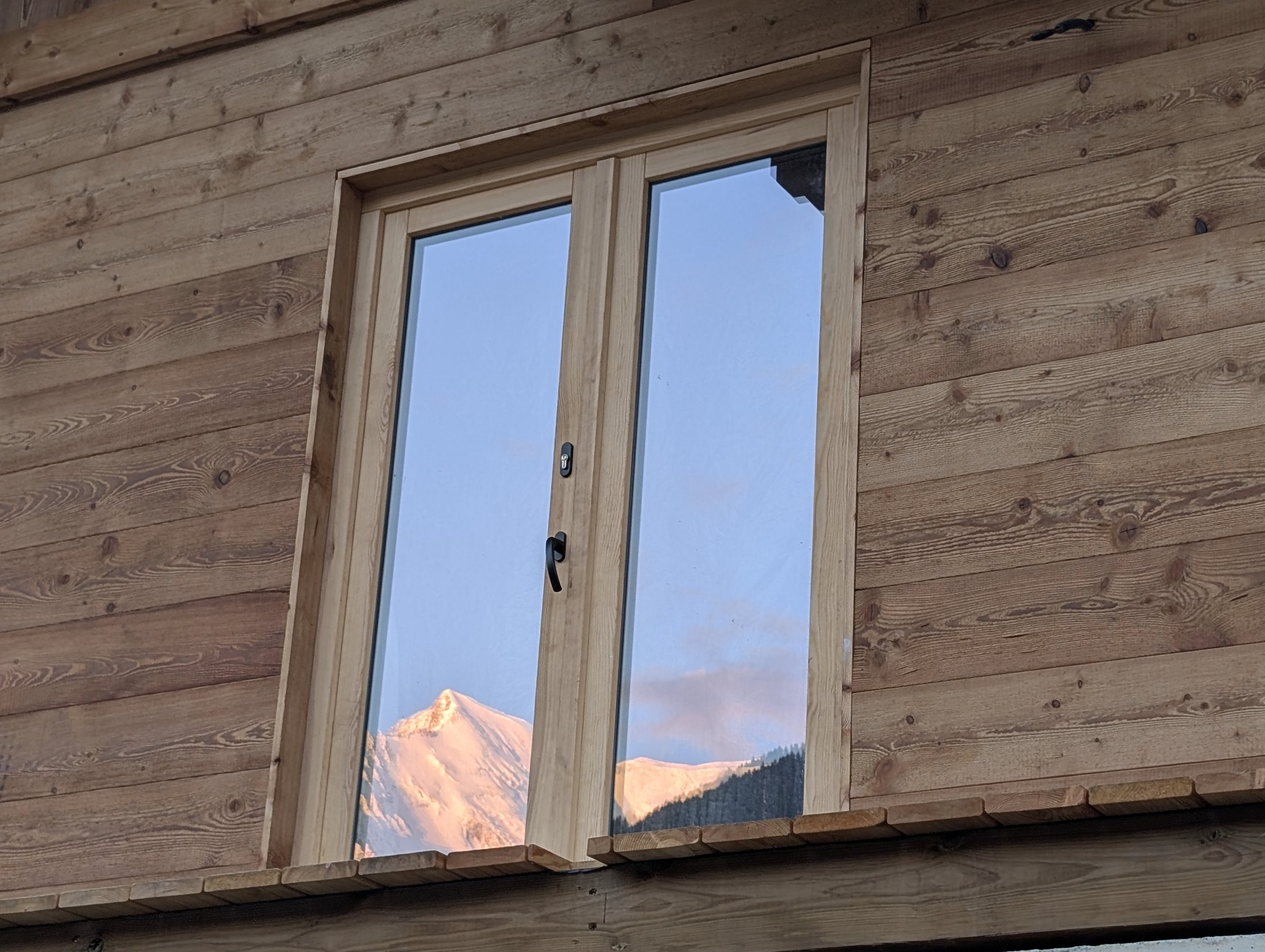Chalet Miage’s French door windows, with the mountains reflected in the glass in the evening sunset