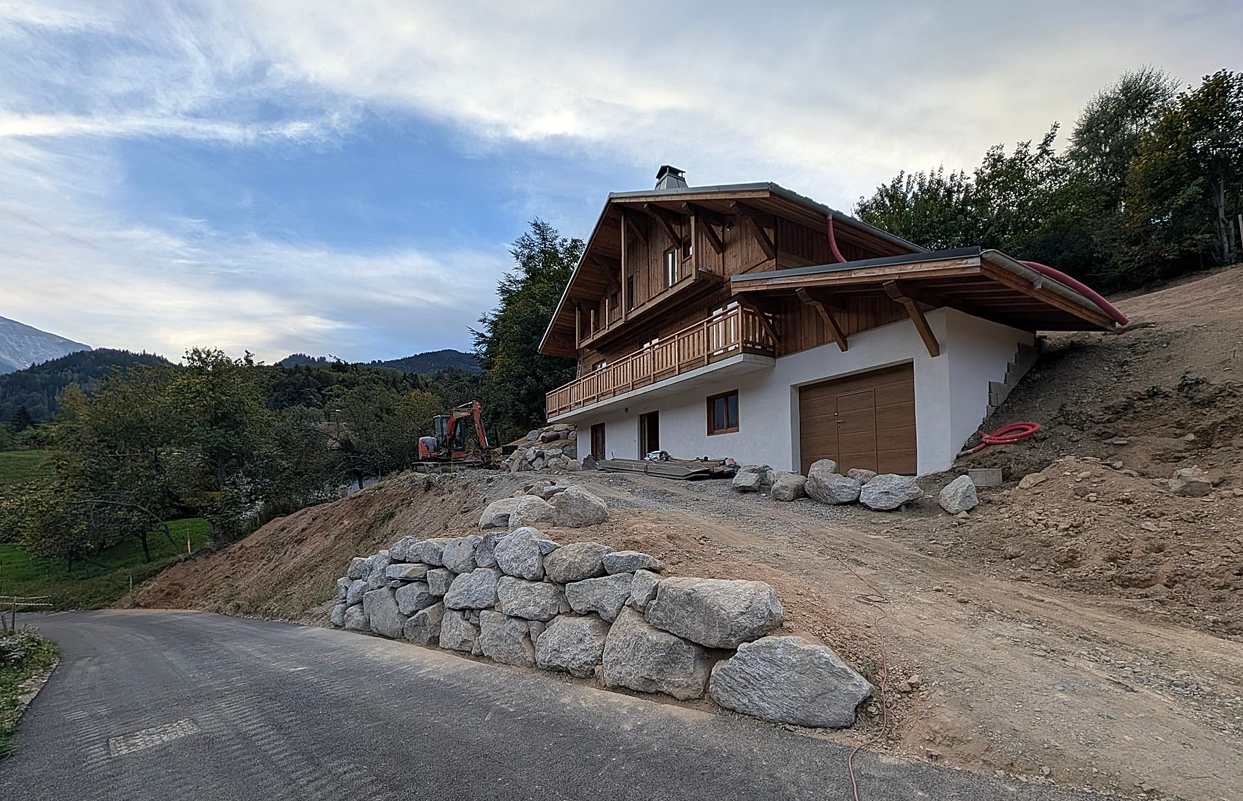 Chalet Miage under construction on its hillside plot, with a stone retaining wall in front