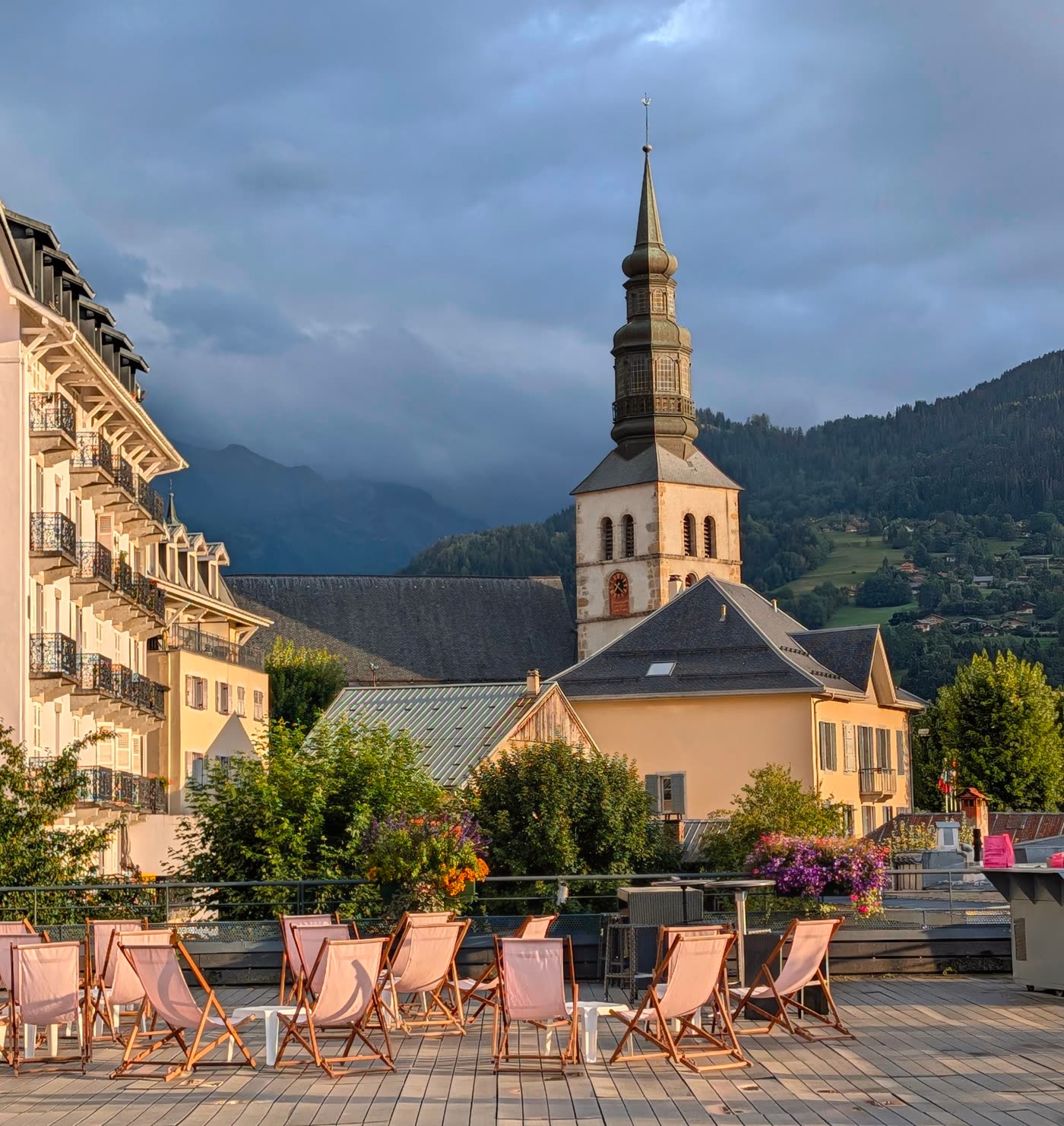 Church tower and rooftops of Saint-Gervais-les-Bains in evening light, with deckchairs in the foreground